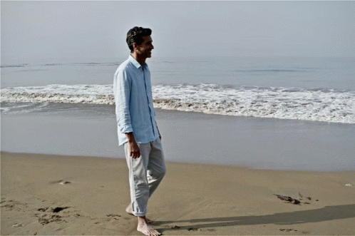a man on a rocky beach looks at the water and walks away