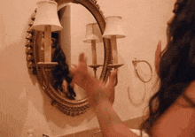 a woman looks at her reflection in a mirror with two lamps