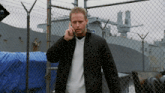a man in a black jacket is talking on a cell phone in front of a fence