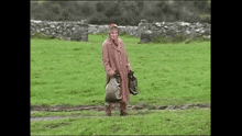 a woman in a pink coat is standing in a field holding a bag .