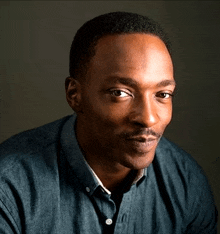 a man in a blue shirt looks at the camera with a serious look on his face