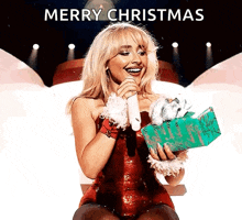 a woman is singing into a microphone while holding a gift box and the words merry christmas are above her