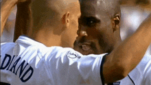 a man wearing a white shirt with the name diand on the back is hugging another man