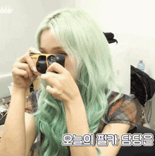 a woman with green hair holds a kodak camera