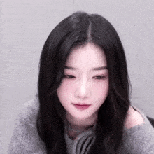 a close up of a woman with long black hair wearing a gray sweater and looking at the camera .