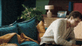 a man in a white sweater sits on a blue couch looking at his phone
