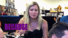 a woman in a black tank top is talking into a microphone with the word because behind her