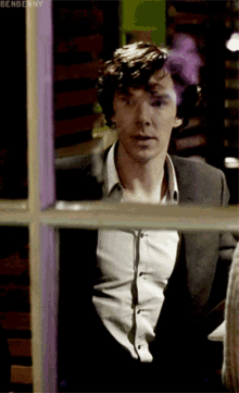 a man in a suit and white shirt looks out a window with benbenny written on the bottom