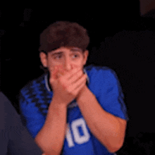 a man wearing a blue shirt with the number 10 on it is covering his mouth with his hands .