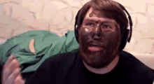 a man with a beard is wearing headphones and has a chocolate mask on his face .
