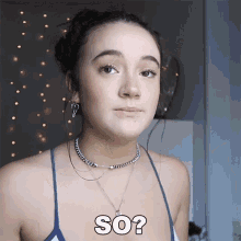 a woman wearing a blue tank top and a necklace says so