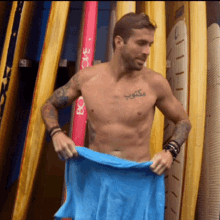 a shirtless man with a tattoo on his chest is holding a blue towel in front of a row of surfboards