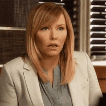 a woman wearing a white jacket and a blue shirt looks surprised