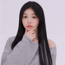 a woman with long black hair wearing a grey off the shoulder top