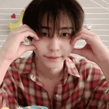 a young man wearing a plaid shirt is making a face with his hands