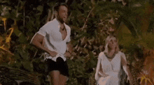 a man in shorts is standing next to a woman in a white dress who is sitting in a chair .