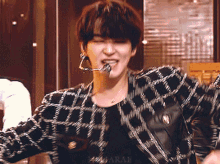 a man wearing a black and white plaid jacket with a microphone in his mouth .
