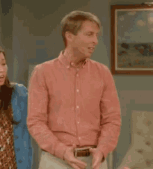 a man in a red shirt is standing in a living room with his hands outstretched .