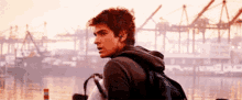 a man wearing headphones and a backpack is standing in front of a large body of water .