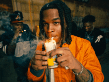 a man in an orange jacket is smoking a cigarette while wearing a hat with the letter a on it