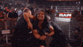 a woman is being held by a man in front of a crowd with a sign that says raw