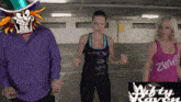 a man in a purple shirt is standing next to two women wearing zumba tops