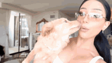 a woman wearing glasses is kissing a small dog
