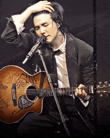 a man in a suit is singing into a microphone while holding a guitar that has the word suck written on it