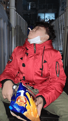 a man in a red jacket is eating a bag of potato chips