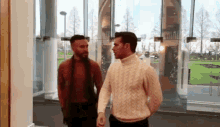 two men standing next to each other in front of a window