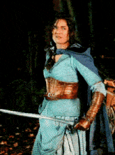 a woman in a blue dress is holding a sword in a dark forest
