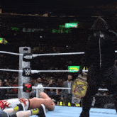 a man in a black hoodie stands in a wrestling ring with a w on the ropes