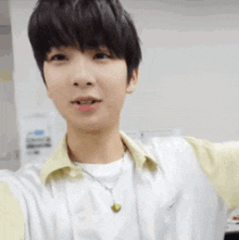 a young man wearing a white shirt and a yellow collared shirt is taking a selfie .