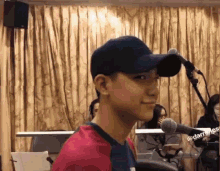 a young man wearing a baseball cap and a red shirt is standing in front of a microphone .