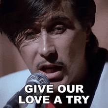 a man singing into a microphone with the words " give our love a try " next to him