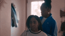 a woman in a blue adidas jacket is putting a braid in another girl 's hair