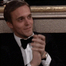 a man in a tuxedo and bow tie holds his hands together