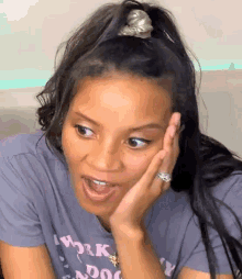a woman with long black hair and a ponytail is making a funny face with her hand on her face .