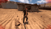 a man in a black jacket is standing in the sand in front of a house