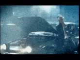 a man is sitting in front of a car with the hood open .