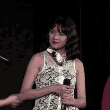 a woman in a white lace dress holds a microphone in her hand