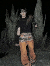 a young man in a black shirt and orange pants is standing in front of a large rock formation
