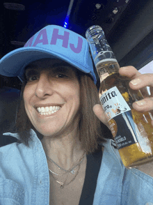 a woman wearing a hat that says ahj holds a bottle of corona beer