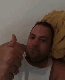 a man in a white tank top gives a thumbs up sign