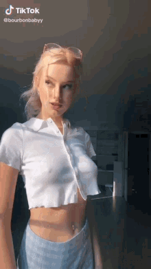 a woman wearing a white crop top and blue plaid shorts is standing in a room .