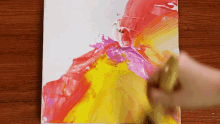 a person is holding a brush over a colorful painting on a table