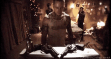 a man is standing next to two guns on a table in a room .