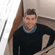 a man wearing a black sweater and a blue scarf around his neck smiles for the camera