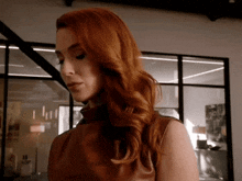 a woman with red hair is wearing a brown leather dress and standing in a room .