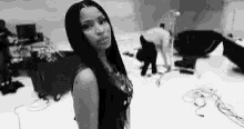 a black and white photo of a woman standing in a room with a man in the background .
